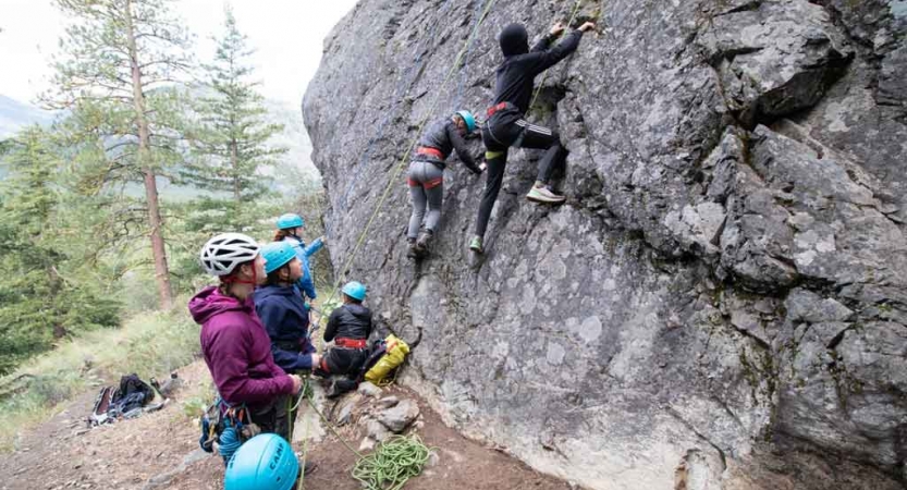 two students climb a rock wall while others look on from below